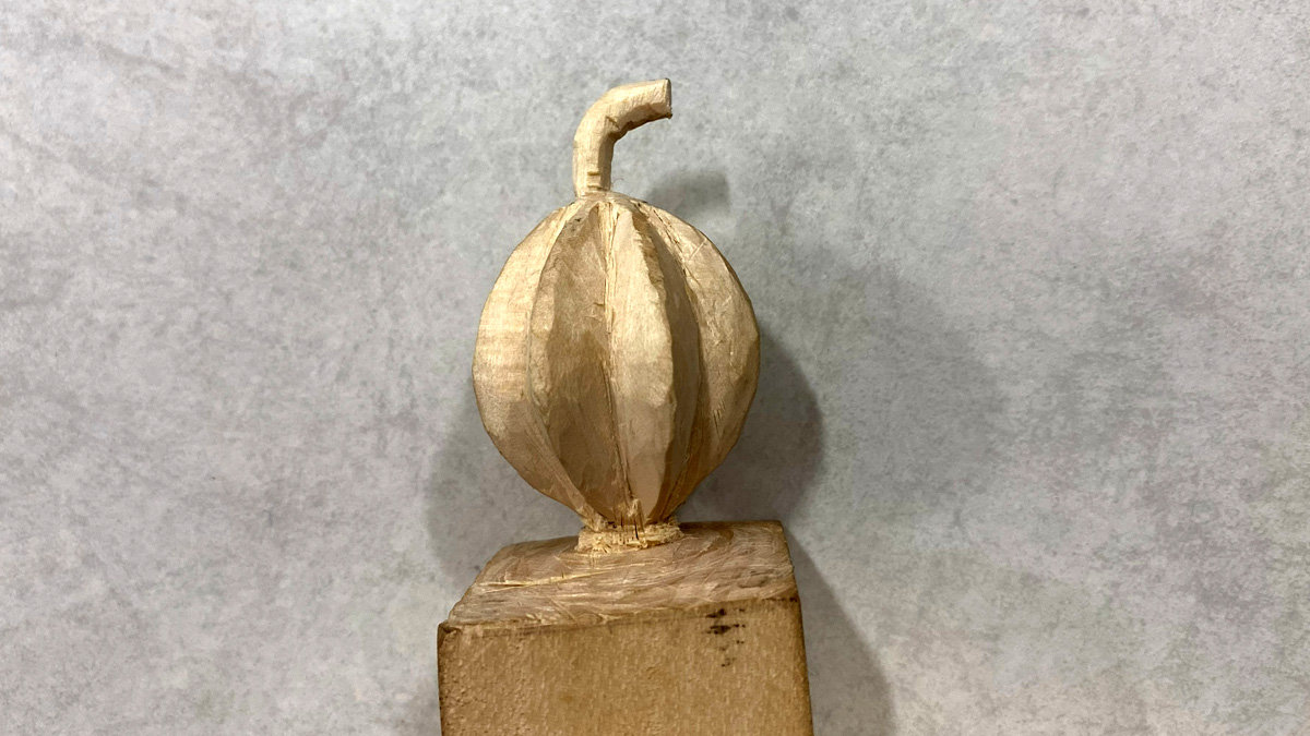 A roughed-out basswood pumpkin carving with a curved stem resting on a block.