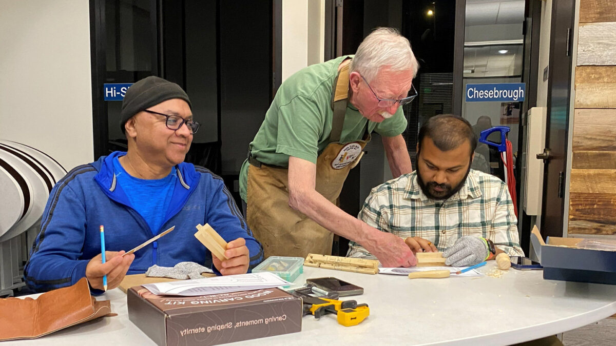 David guides Avaneesh in carving a wooden chain from a block of wood.