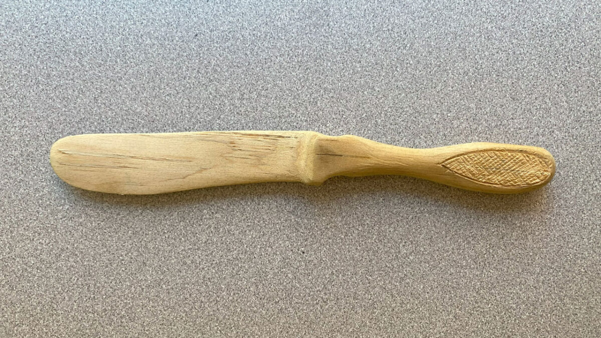 A butter spreader carved from basswood. A handle is decorated with a checkering pattern.