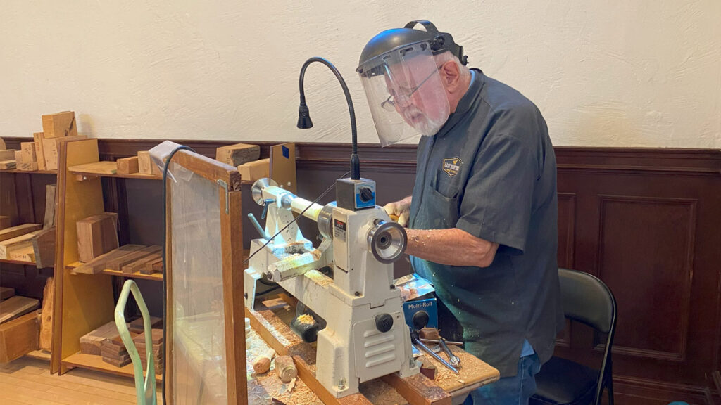 Dave Boles demonstrated spindle turning at the 2025 TVC Woodcarving Show. The photo shows Dave behind a mini lathe with a protective safety screen.