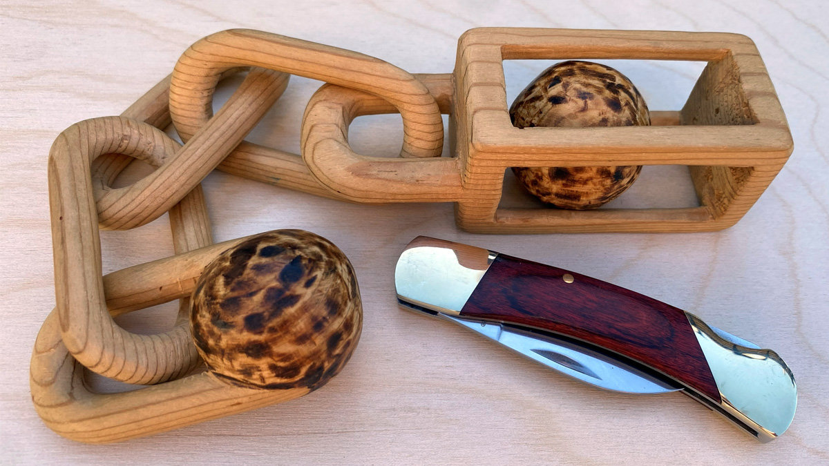 A wooden chain carved by David Osterlund has a ball in a cage on one end. The image also contains a folding knife.
