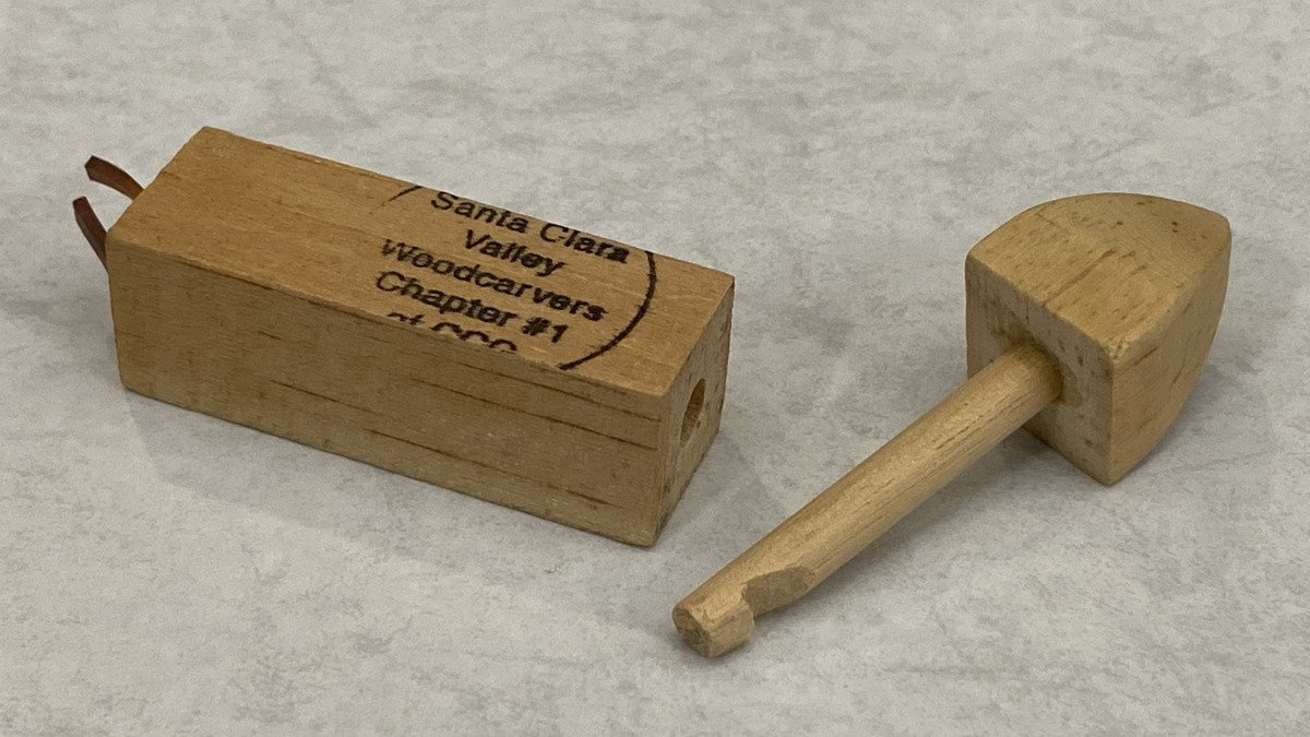Hand-carved wooden puzzle by David Osterlund featuring a small mallet and a branded block for the Santa Clara Valley Carvers, displayed at a club meeting in San Jose, CA.