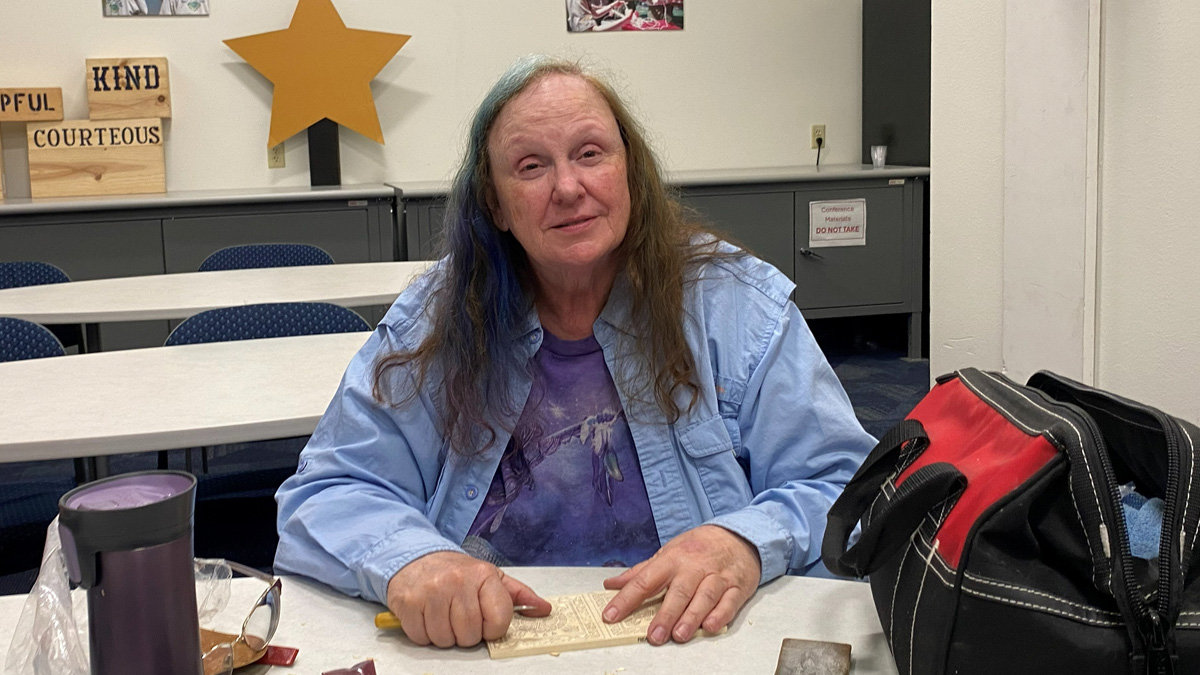 Debbie Mize is chip carving a piece of basswood at a table.