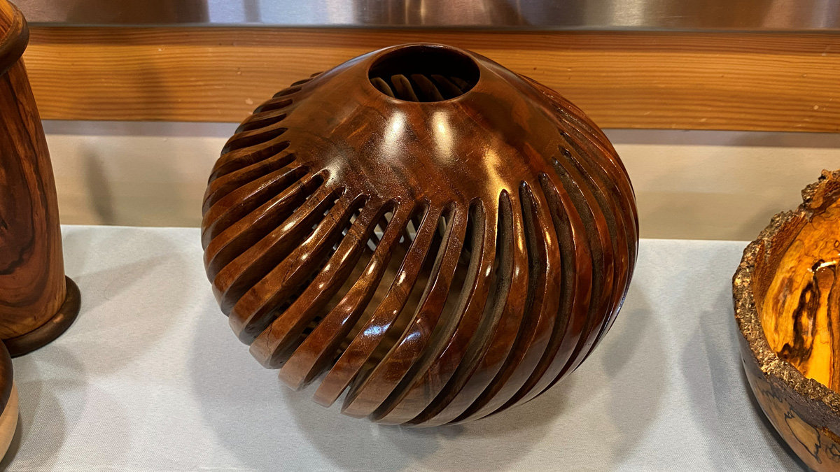 A dark walnut vessel featuring a spiraling ribbed design and internal vanes visible through the top opening.