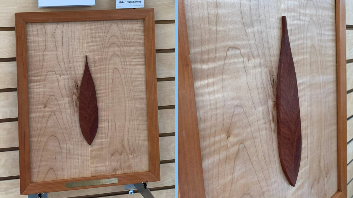 Two views of a framed woodworking art piece by Frank Ramsay. The artwork features a dark reddish-brown, leaf-shaped piece of wood mounted vertically on a light-colored, figured wood panel. The left image shows the full piece in its medium-brown frame with a maker's label at the top. The right image provides a close-up view, emphasizing the texture and grain of the dark wooden leaf against the wavy grain of the background wood.