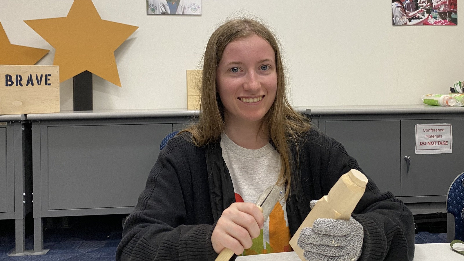 Hedy Gaff, a new Santa Clara Valley Carvers member, uses a carving knife and cut-resistant glove to carve a wooden pumpkin at a September 2026 meeting in San Jose, CA.