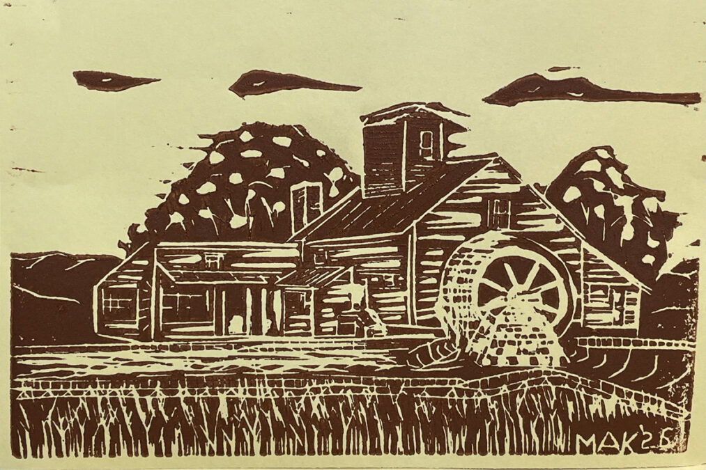 A brown linoleum block print depicting a wooden grist mill with a large water wheel on the right side. The scene features stylized trees in the background, clouds in the sky, and tall grass or reeds in the foreground. The artwork is signed "MAK '26" in the bottom right corner.