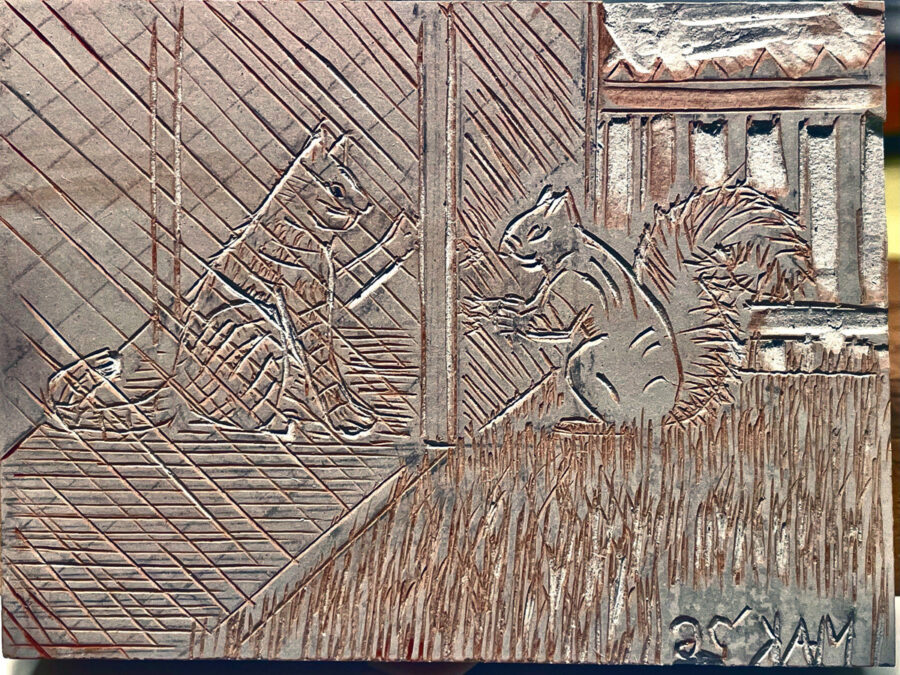 A linoleum relief carving block by Jordan Makower titled "Lunch Block," featuring a striped cat sitting on the left facing a squirrel standing on its hind legs on the right; they are separated by a vertical post with grass carved at the bottom and diagonal siding in the background.