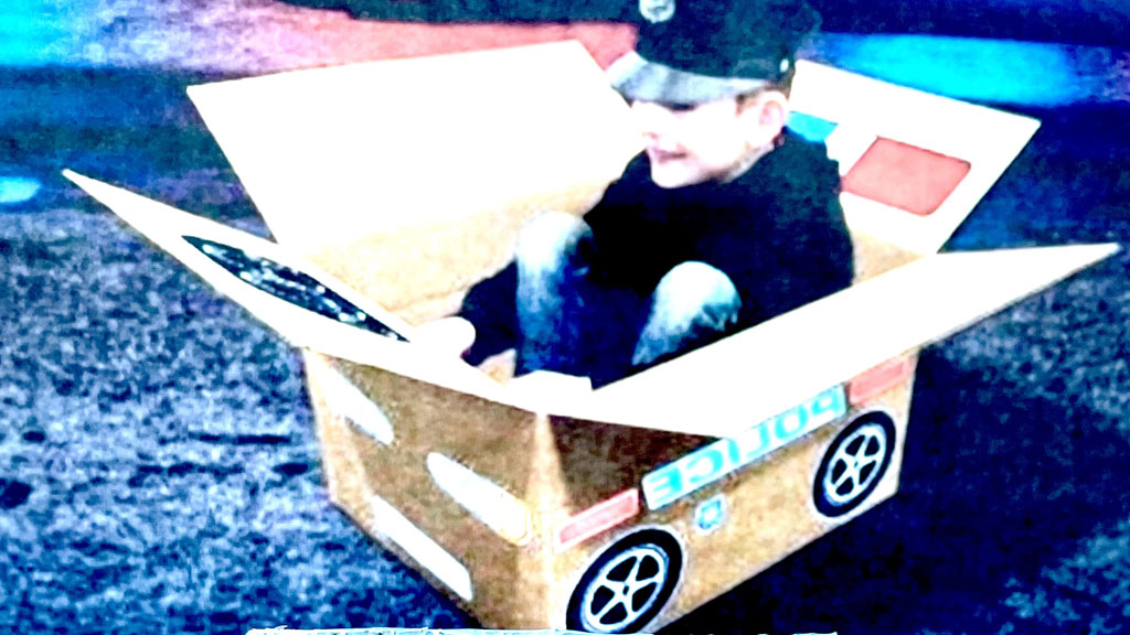 The photo depicts a child in a cardboard box pretending to be a car.