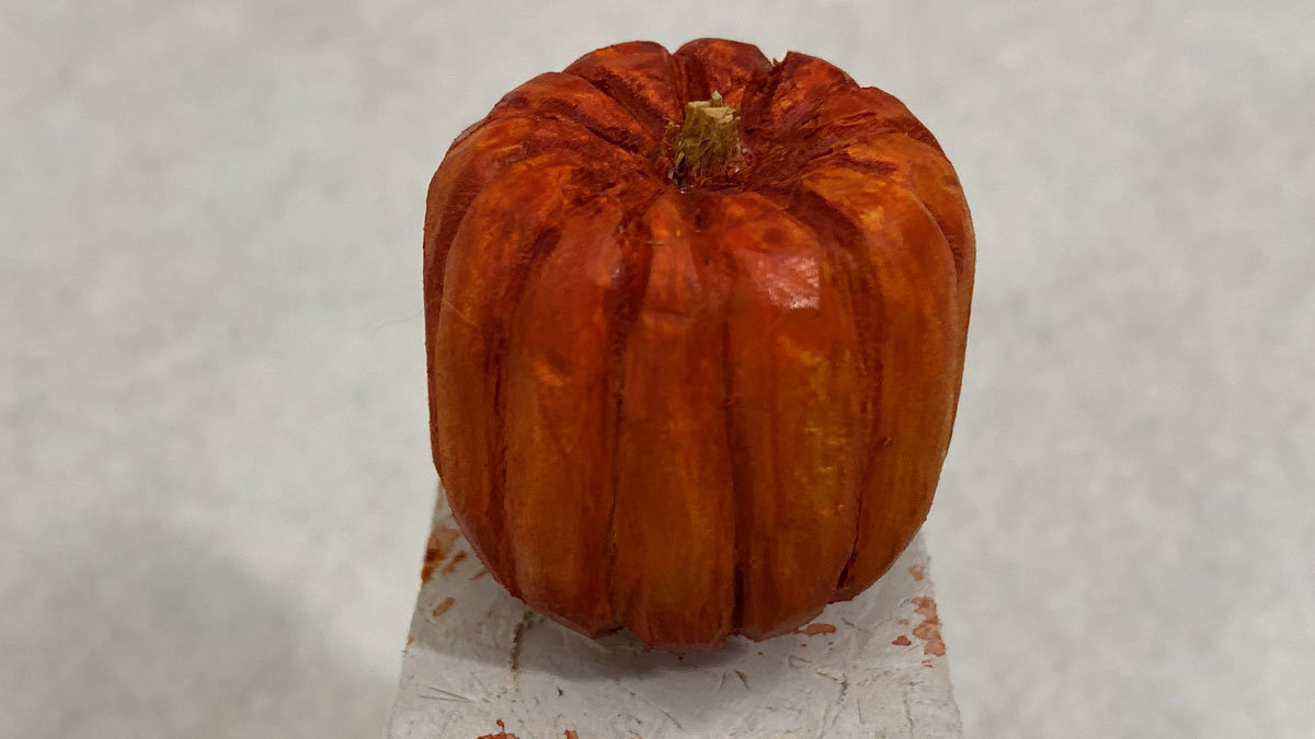 A small pumpkin carved from basswood and painted bright orange. It is 1.5" in diameter.
