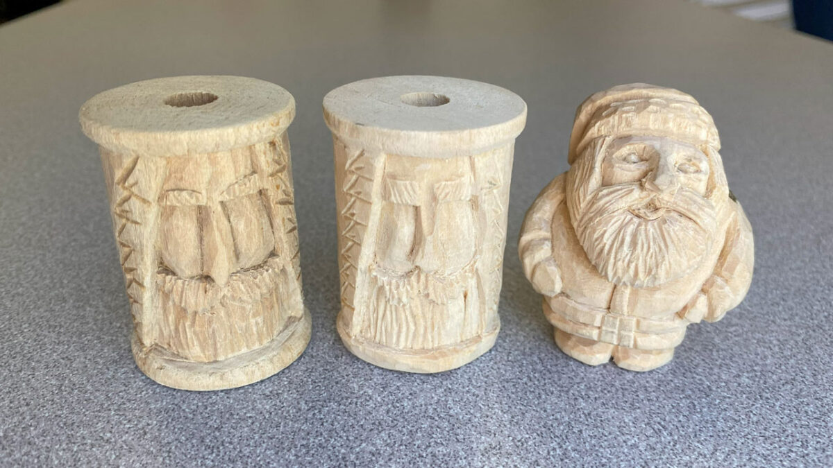 Two wooden spools with carved faces and a carved Santa from basswood.
