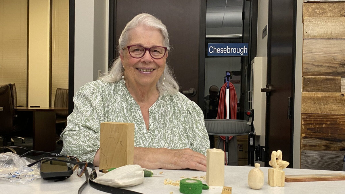 Martha Hanisch smiles at a table of woodcarving projects, including a basswood block and a wooden pumpkin, during a Santa Clara Valley Carvers meeting.