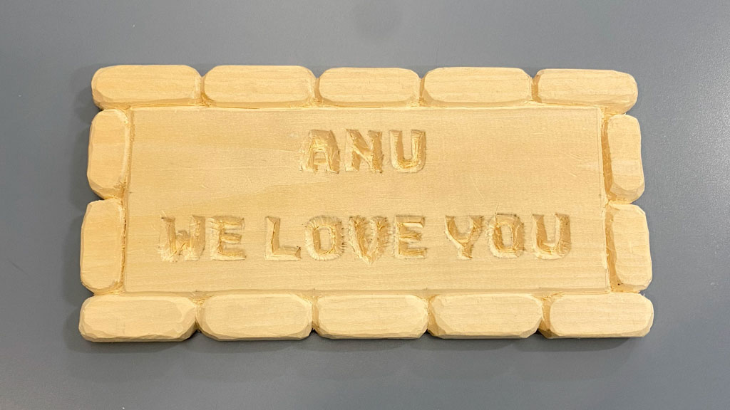 A wooden plaque with a message "Anu we love you" carved from a basswood board.