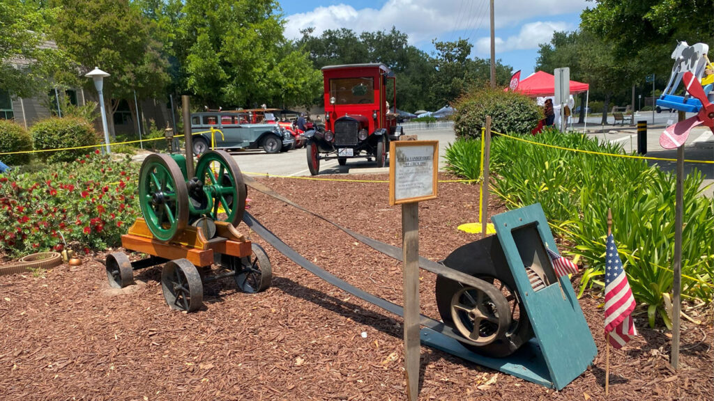 Antique water pump with antique cars in the background at the Saratoga Blossom Festival, 2025.