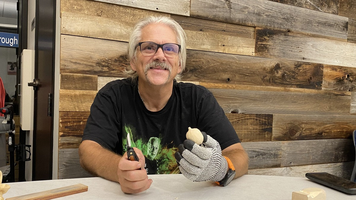 Peter Hanisch smiles while holding a carving knife and an unfinished wooden pumpkin at a Santa Clara Valley Carvers meeting in San Jose, California.