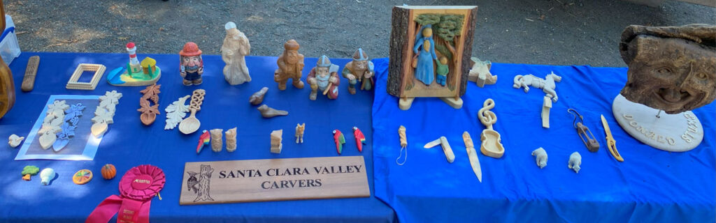 Table with carvings: carved spoons, vikings, small animals, and other whittling projects.