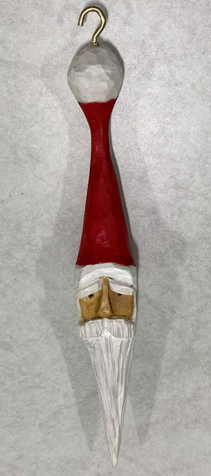 A Christmas decoration carved and painted by Pranay. It consists of a Santa head in a hat. The long hat and beard form an elongated ornament resembling an icicle.