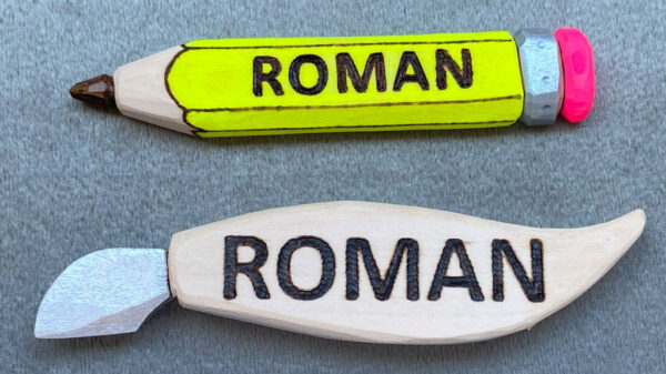 Two carved name badges: one carved in the shape of a pencil and the other in the shape of a chip carving knife.