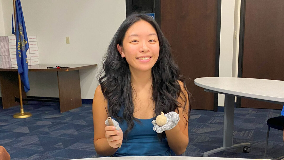 Sarah Liu is holding a woodcarving knife and a small pumpkin that she carved from basswood.