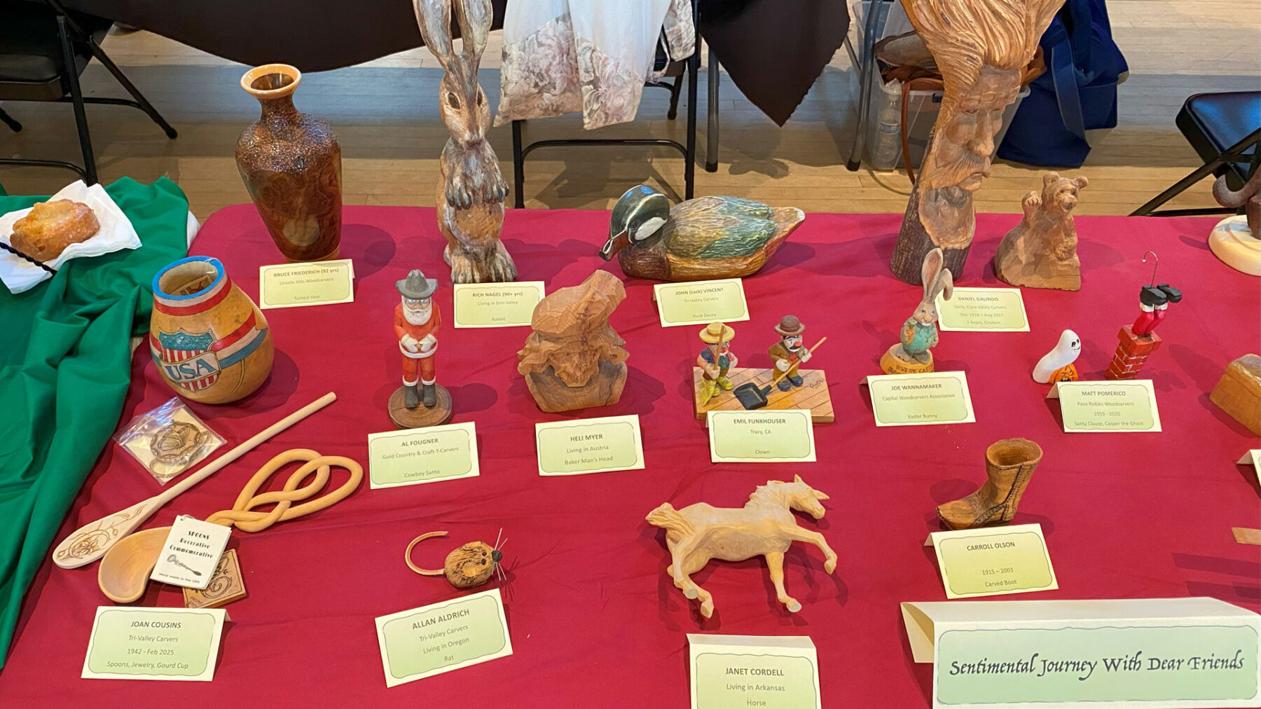 A table full of woodcarvings from several artists: carved animals and caricatures.