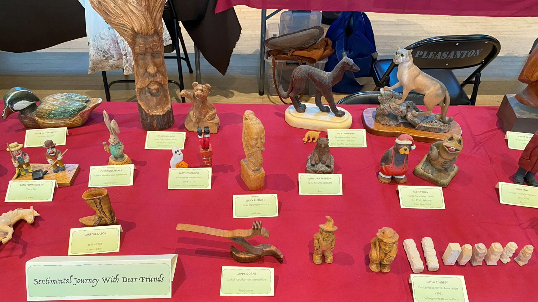A table full of woodcarvings from several artists: carved animals and caricatures.