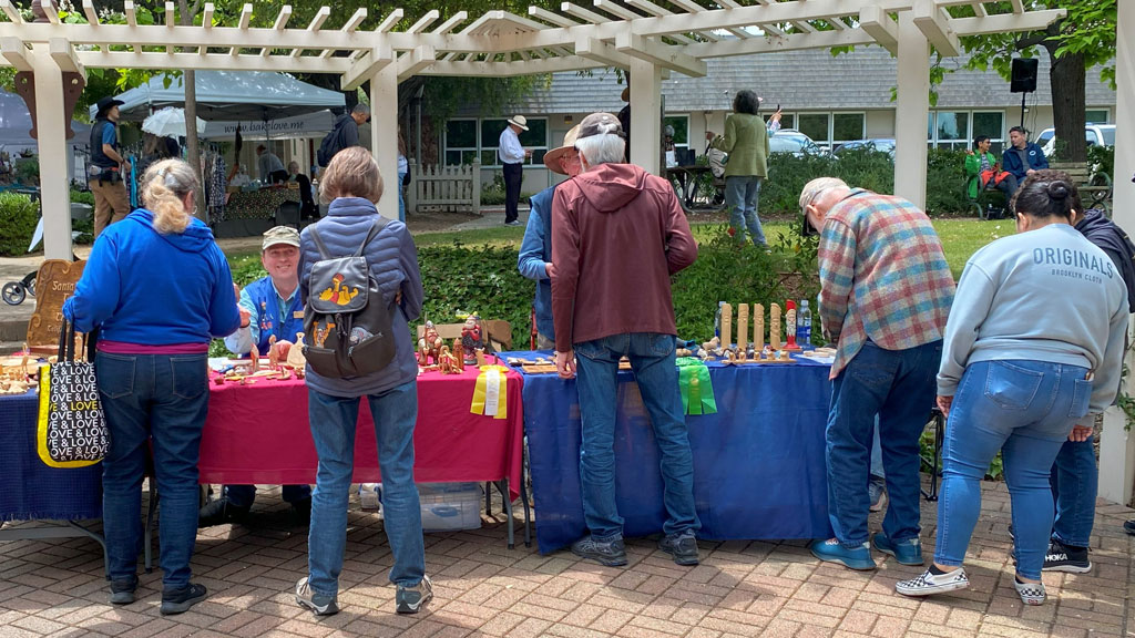 Woodcarving booth at Saratoga Blossom Festival. There are many visitors near the tables.