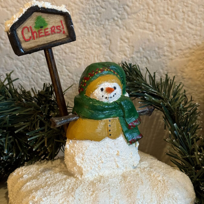 Artfully painted wooden snowman standing with the "Cheers!" sign.