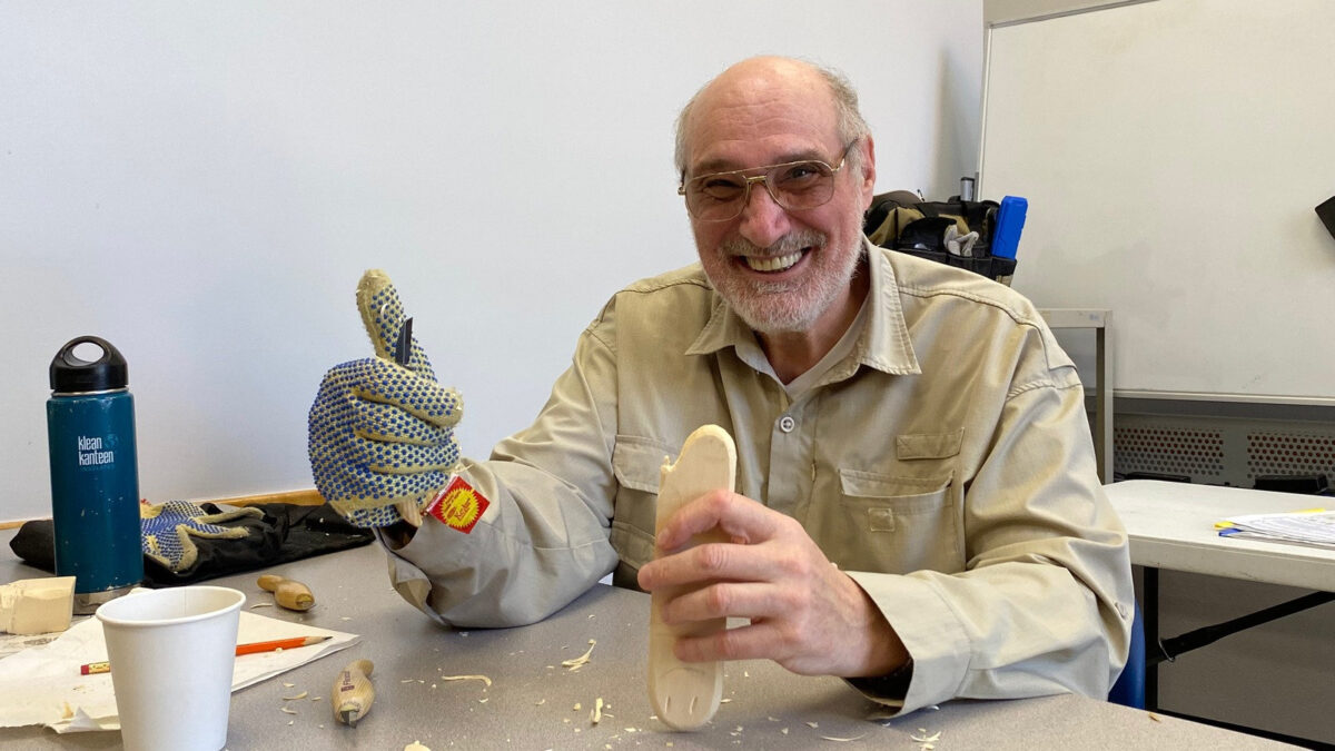 Smiling woodcarver Sorin Papuc holds up an early stage of a ghost carving, and both he and the carving show a thumbs-up, during a Santa Clara Valley Carvers workshop in Los Gatos, California.