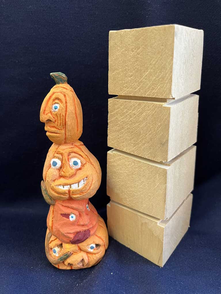 Four Halloween pumpkins stacked together, one on top of the other. Also, shown a piece of basswood to carve the pumpkins. This is a project for woodcarving class on wooden pumpkin carving.