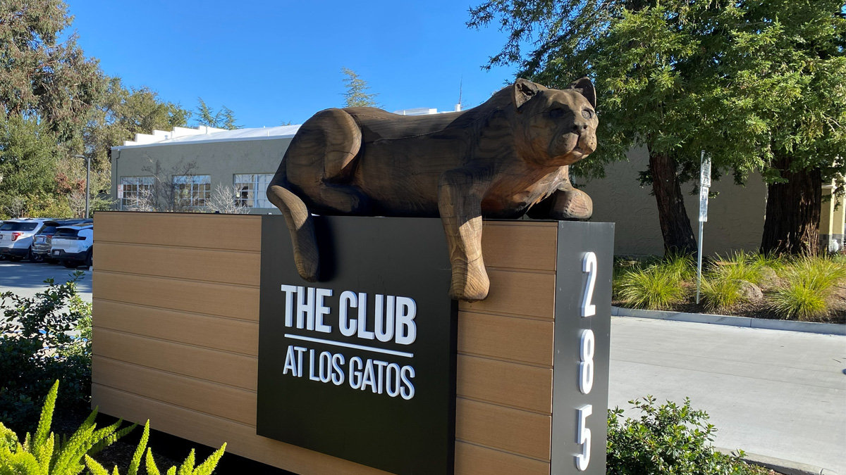 A large wooden sculpture of a mountain lion resting on top of an entrance sign.