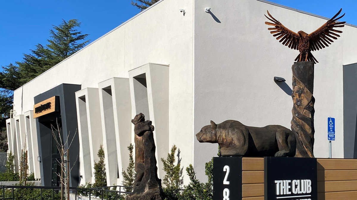 Large wood sculptures of an eagle atop a totem pole, a standing bear, and a resting mountain lion outside the entrance to The Club.
