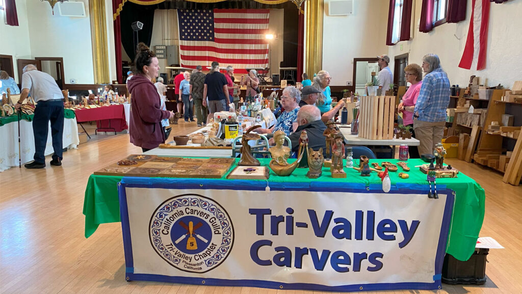 Woodcarving show visitors between tables with woodcarving projects during the Tri-Valley Carvers show in September 2025.