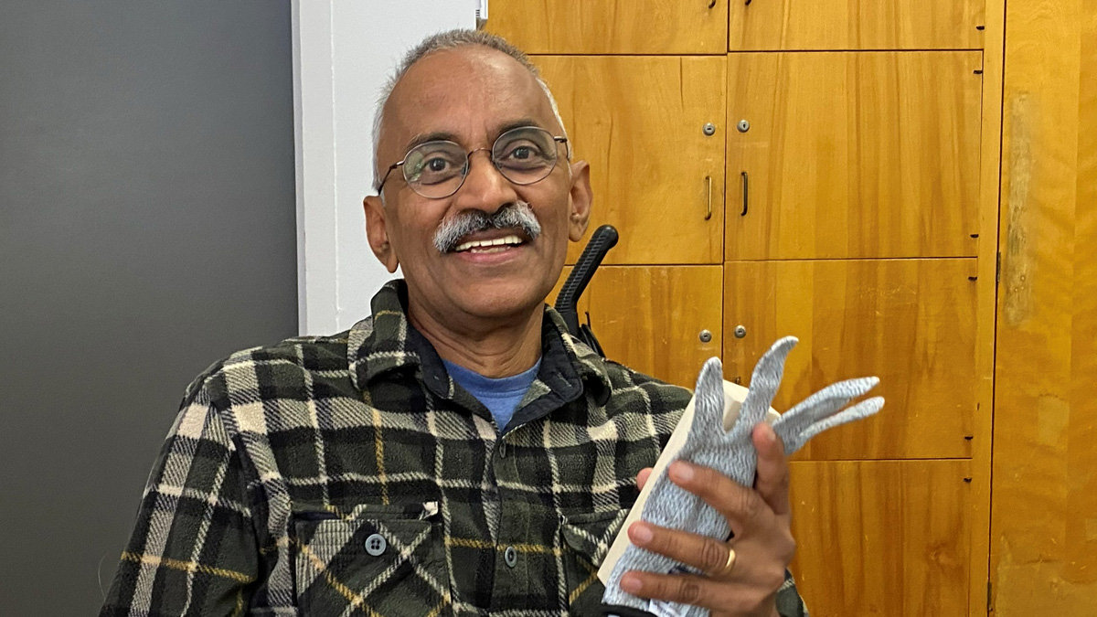 Santa Clara Valley Carvers member Udaya Rangaswamy smiles while holding a basswood block and a cut-resistant glove.
