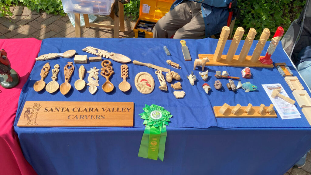 Whittling projects, including carved spoons, lie on the display table at the Saratoga Blossom Festival, 2025.