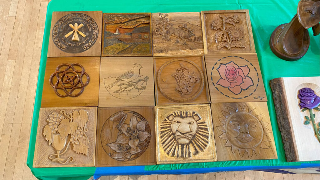 A wooden quilt consists of 12 square pieces with various relief decorations carved by members of the Tri-Valley Carvers club.