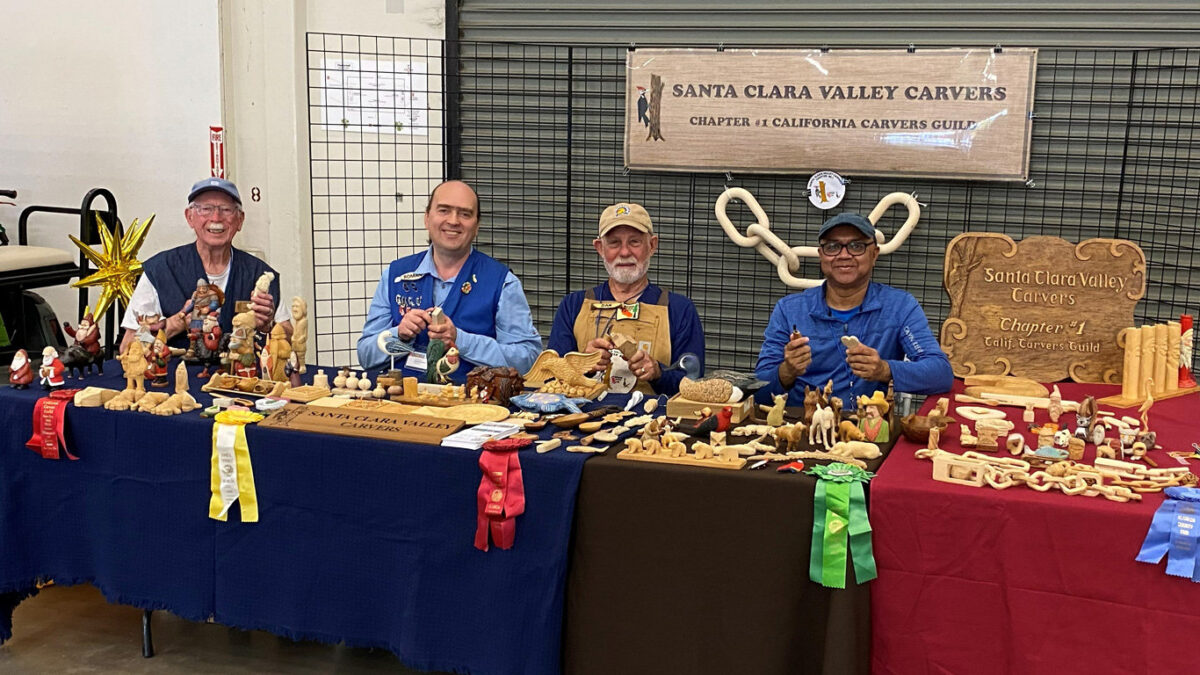 Santa Clara Valley Carvers members David Osterlund, Roman Chernikov, Dan Brady, and Nitin Varshney demonstrate woodcarving and display intricate carvings and wooden chains at the 2026 Santa Clara County Fair.