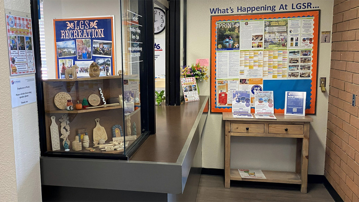 A glass display case at LGS Recreation features basswood carvings, including relief paddles and turning samples, next to community bulletin boards.