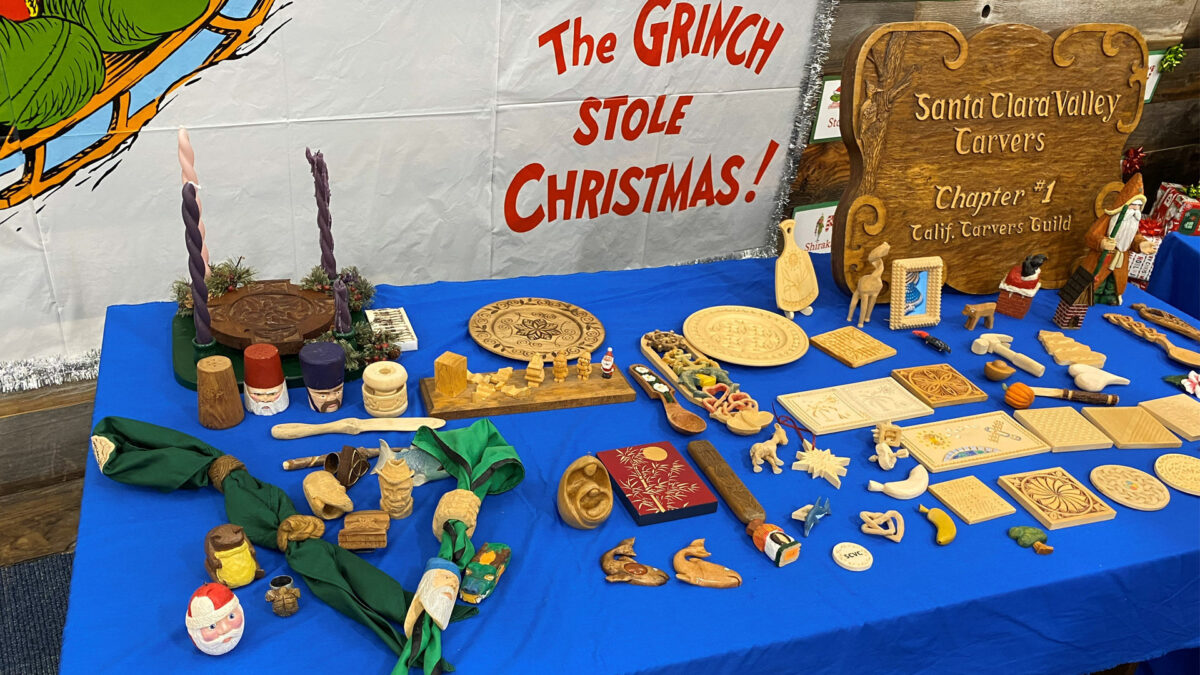 A woodcarving winter holiday display table with various handmade projects, including wooden neckerchief slides.