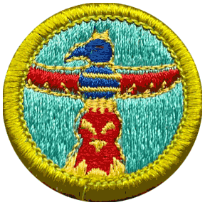 Circular embroidered patch with a yellow border. The center features a stylized bird figure resembling a wood carving in blue and red against a teal background. This is the Woodcarving Merit Badge from Scouting America. Scouts earn this badge after mastering knife safety and carving techniques.