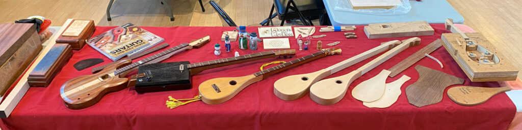 A table with handmade music instruments and whittled snowmen carved by Morgan Heskett. Morgan demonstrated his projects at the 2025 TVC Woodcarving Show in Pleasanton, CA.