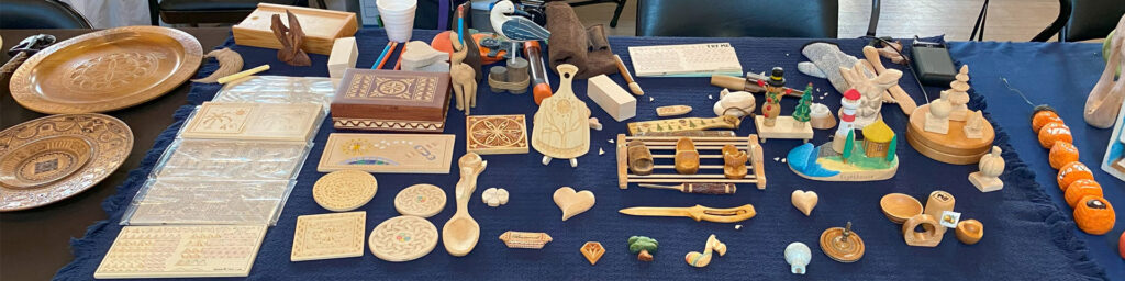 A table with chip carving and whittling projects carved by Roman Chernikov. The woodcarvings were on display at the Tri-Valley Carvers woodcarving show in Pleasanton in September 2025. Visit Roman's website https://readntry.com for more of his carving projects and chip carving patterns.