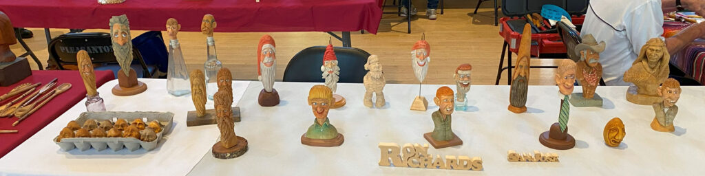 A table with dozens of wooden caricatures carved by Ron Richards at the 2025 TVC Woodcarving Show in Pleasanton, CA.