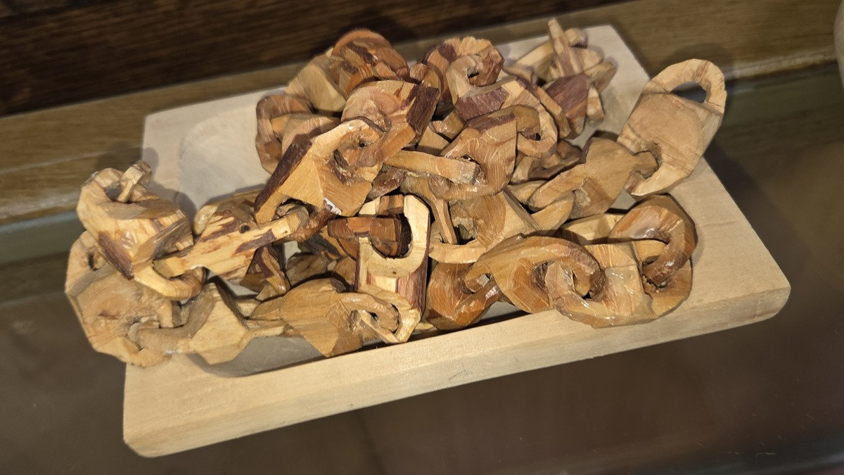 Intricate interlocking wooden chain links carved from a single branch, displayed on a light-colored tray in a museum in Drumheller, Canada.