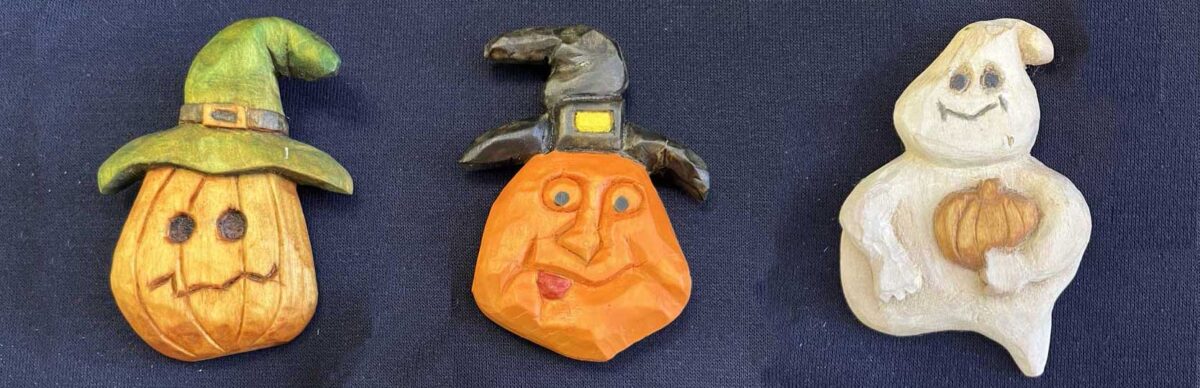 The pumpkin carving workshop featured image shows two wooden pumpkins in hats and smiley ghost that holds a miniature pumpkin.